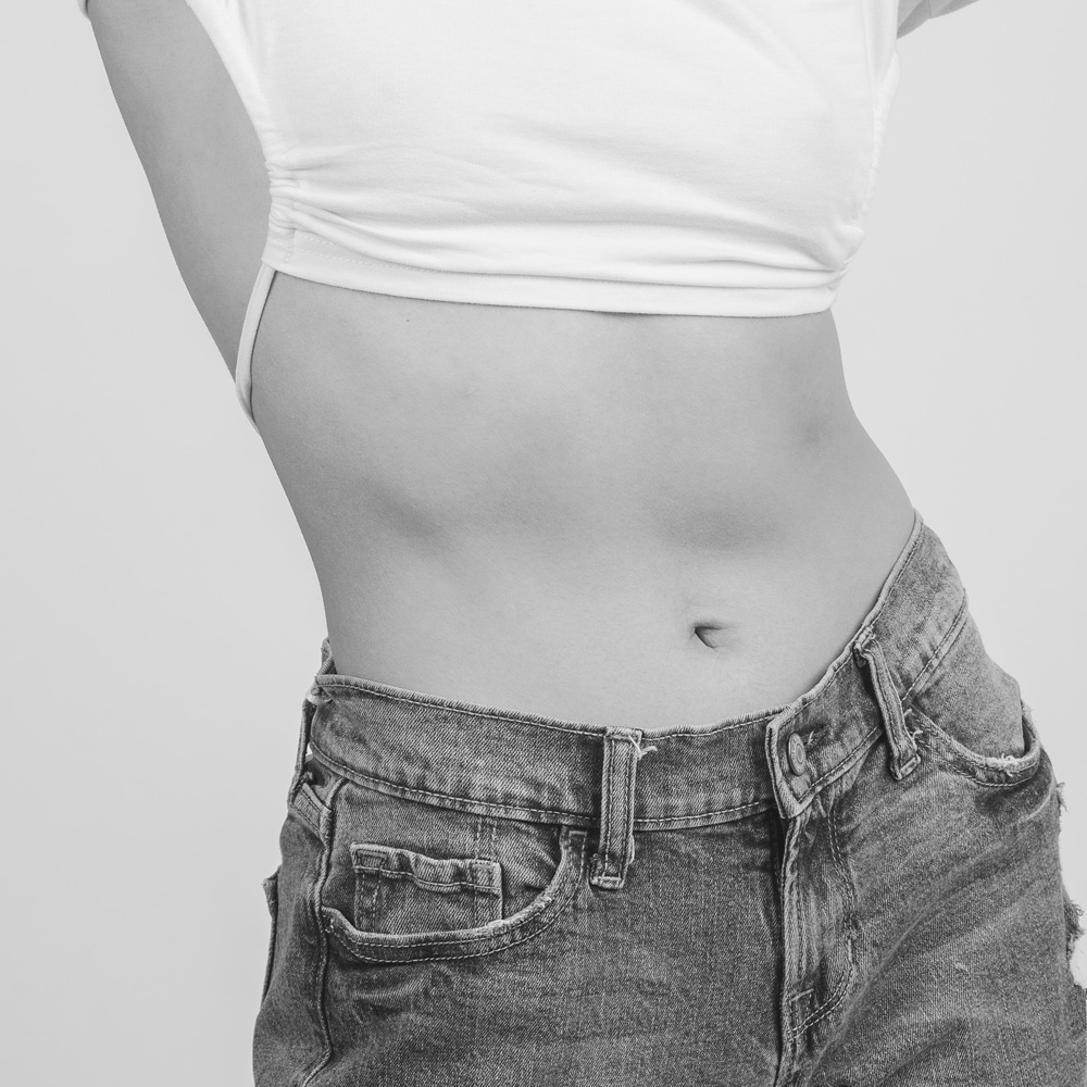 close up of a white woman's flat stomach wearing jeans and white top