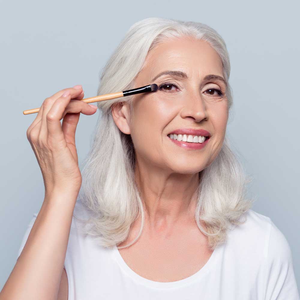 image of an older white woman applying eye shadow