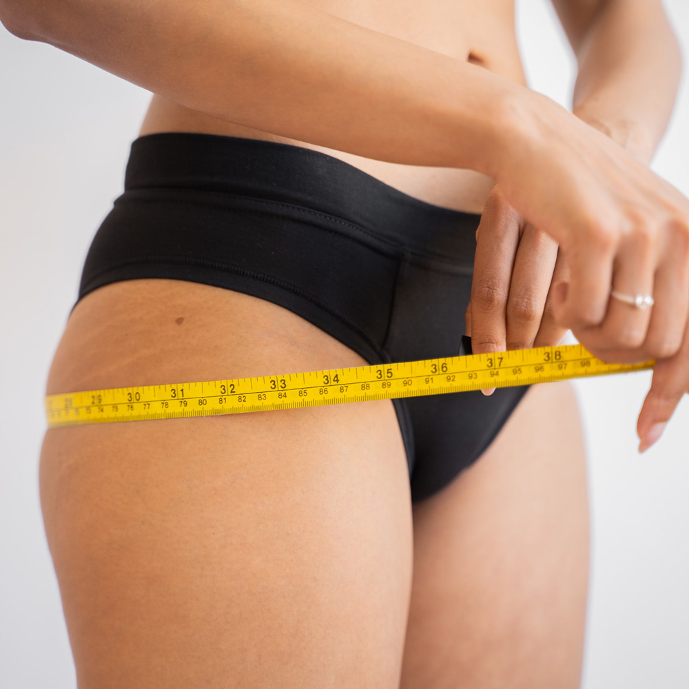 image of a woman in her underwear measuring her thighs with a tape measure